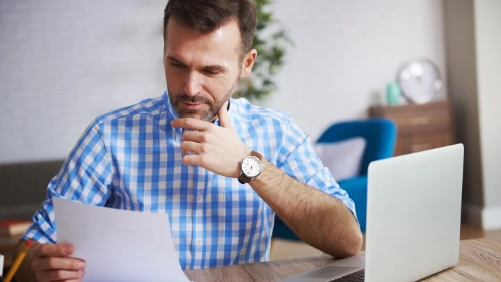 Man looking at document with a laptop to the side