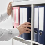 Hand reaching for a file on a shelf full of files