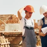 Two builders looking over a document whilst on a building site.