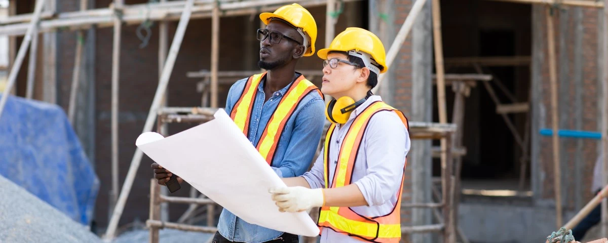 Two men at a construction site, holding a floor plan and looking up