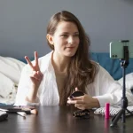 Lady filming in her living room with her smart phone on a tripod on her coffee table.