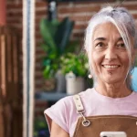 Older lady smiling in front of some plants, presumably a plant shop