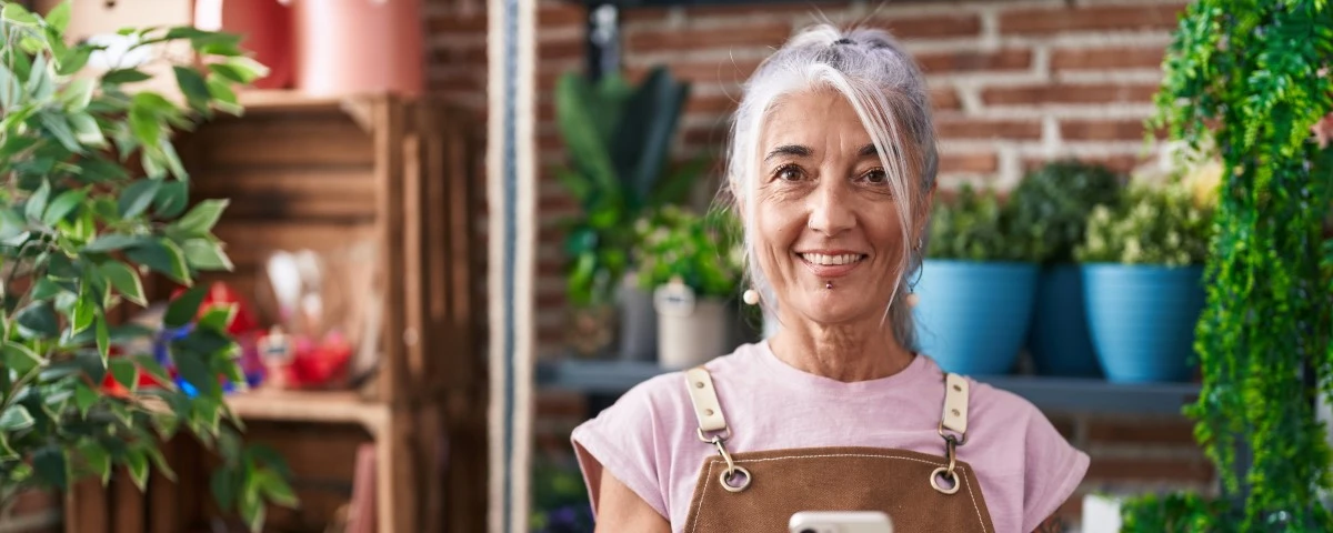 Older lady smiling in front of some plants, presumably a plant shop