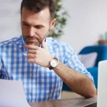 Man looking at document with a laptop to the side