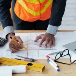 Someone in a suit and high vis vest working on a blueprint