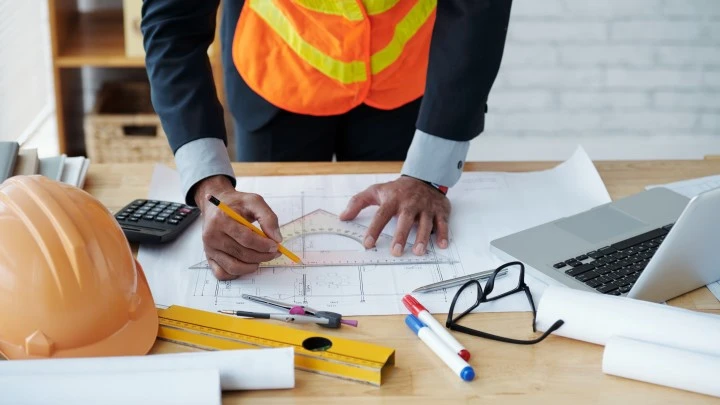 Someone in a suit and high vis vest working on a blueprint