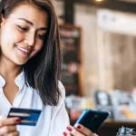 Lady in a coffee shop holding a bank card and phone