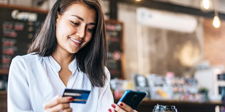 Lady in a coffee shop holding a bank card and phone