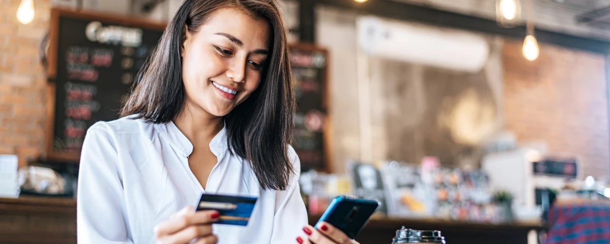 Lady in a coffee shop holding a bank card and phone