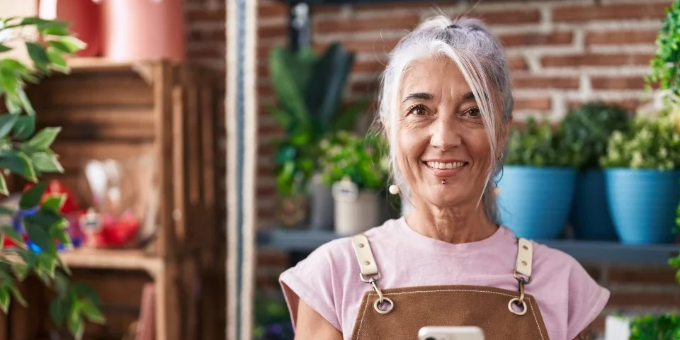 Older lady smiling in front of some plants, presumably a plant shop