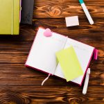 A notebook laid out on a desk with post-its and pens.